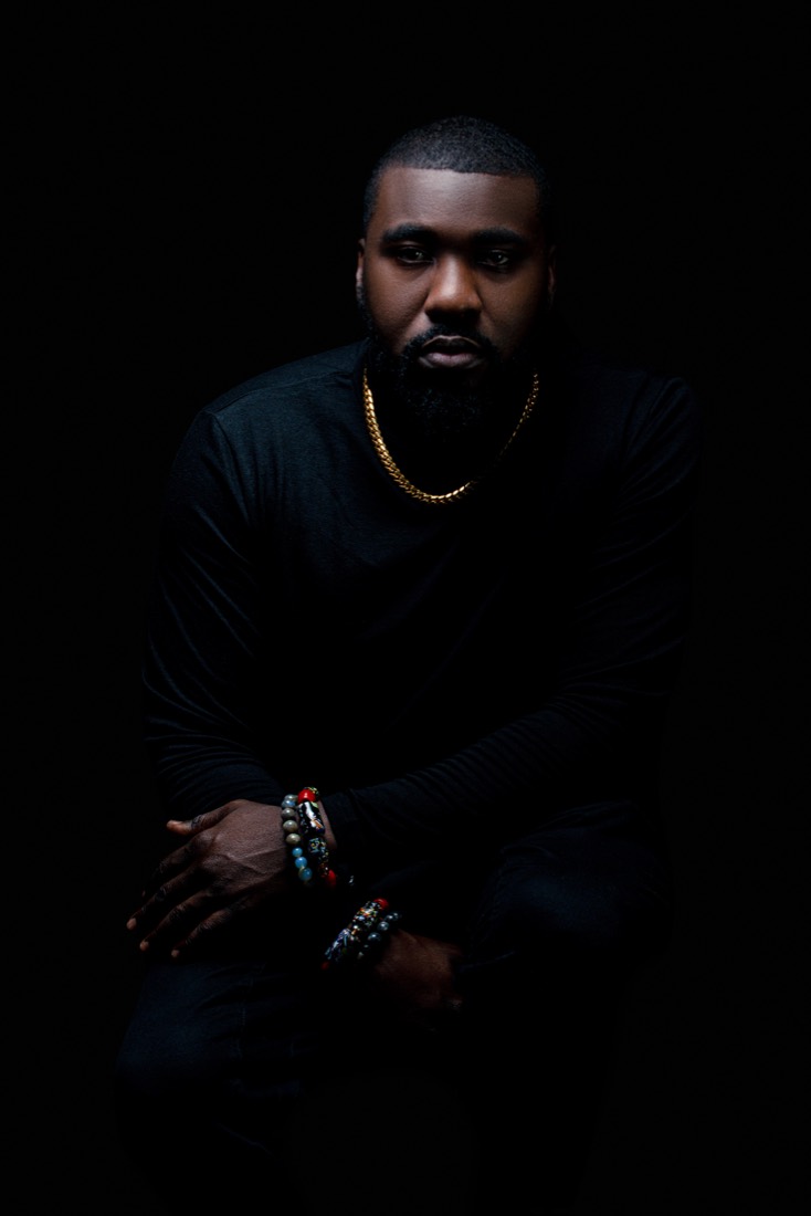 Low-key portrait of DJ OMG PRINCE in all black with a gold chain